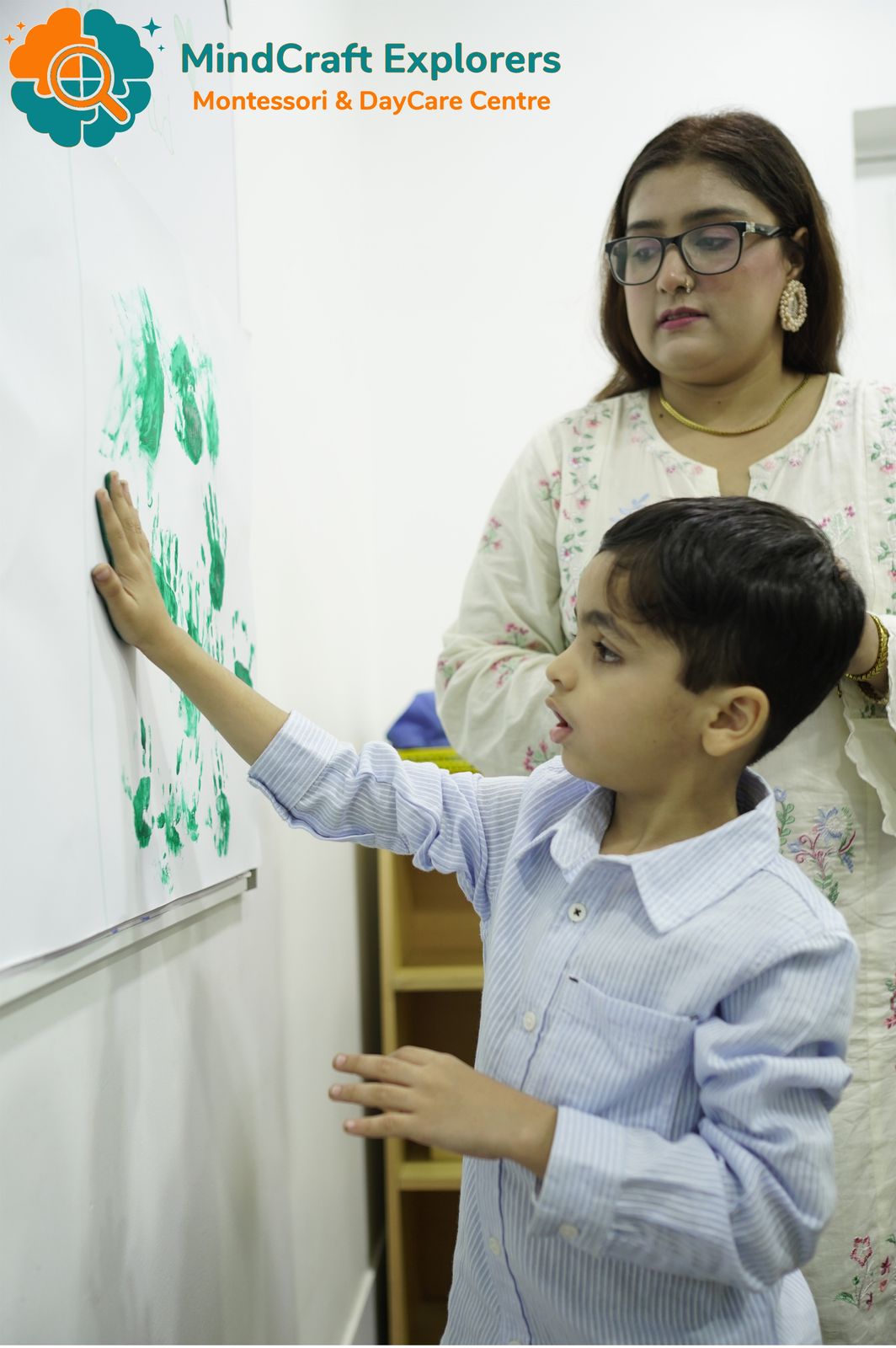 A boy adding his green handprint to a class mural