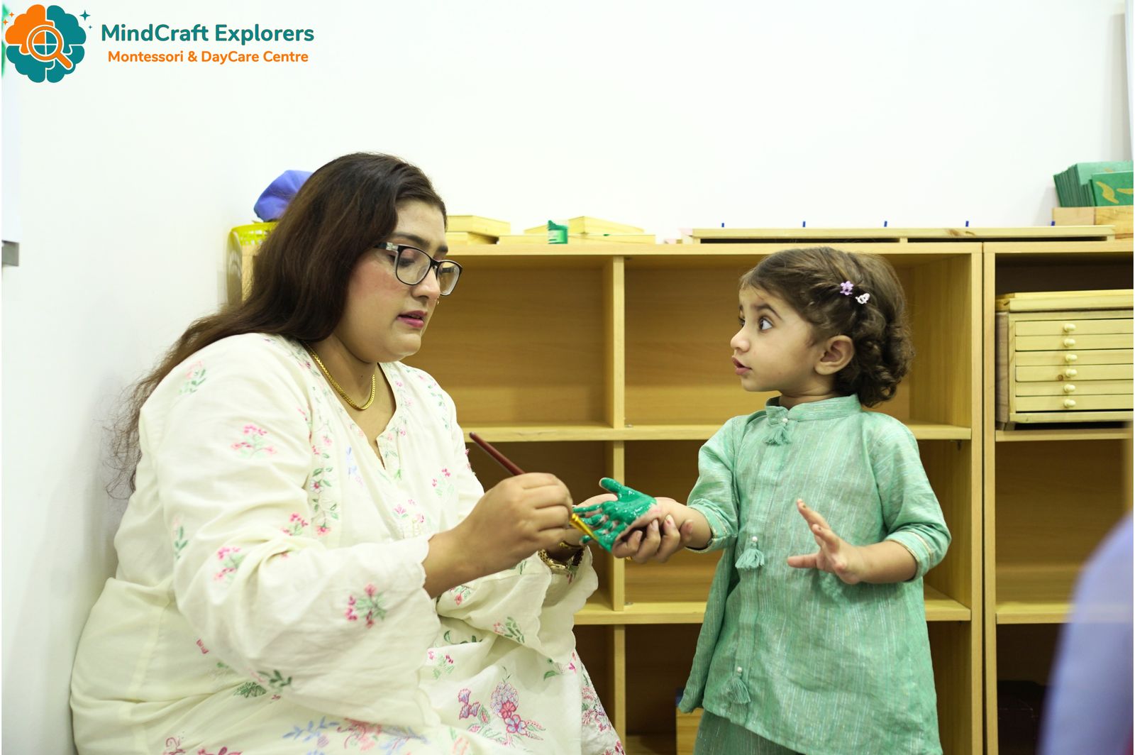 A teacher working with a young girl beside the classroom shelves